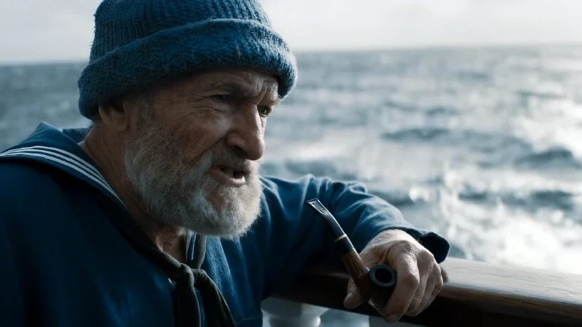 An older man in a knit cap smokes a pipe in a cinematic close-up.