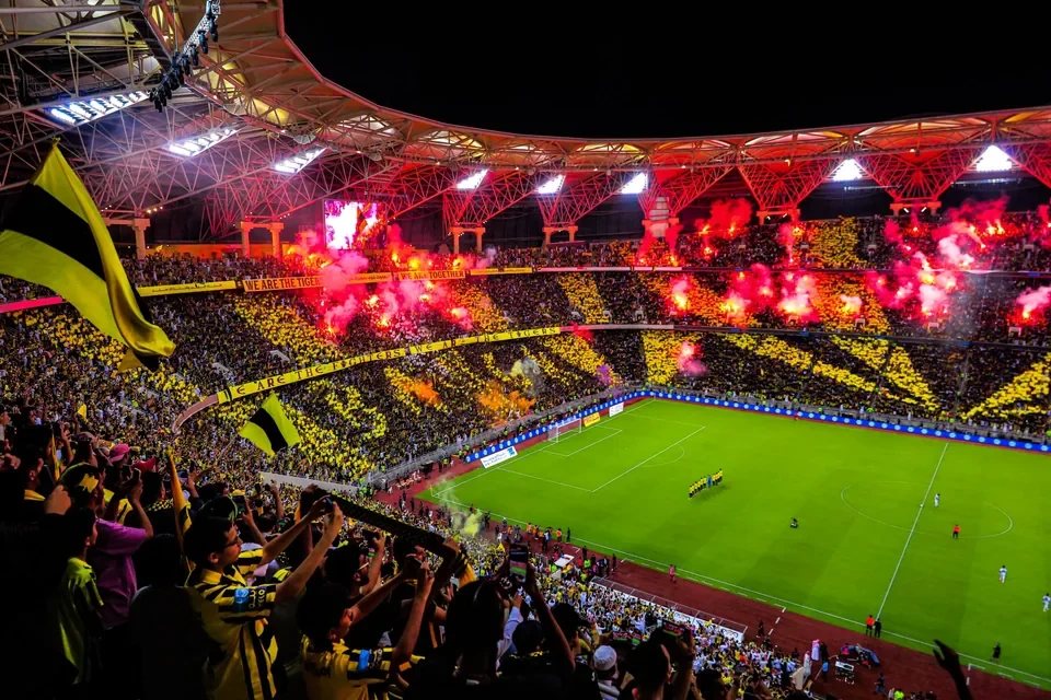 Al-Ittihad supporters fill a stadium with yellow and black banners during a football match.