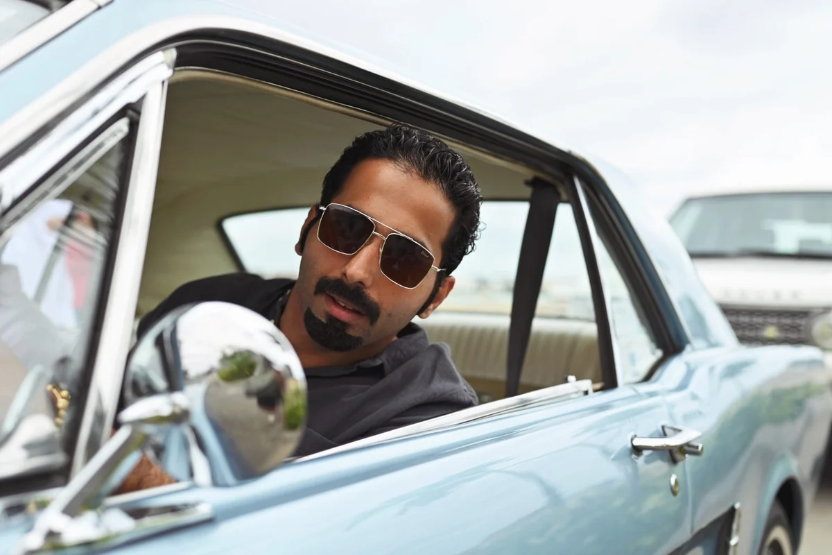 Fahad Al-Qahtani leans from the window of a light blue classic car.