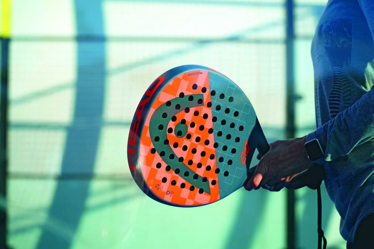 A brightly colored padel racket held against a pale green court.