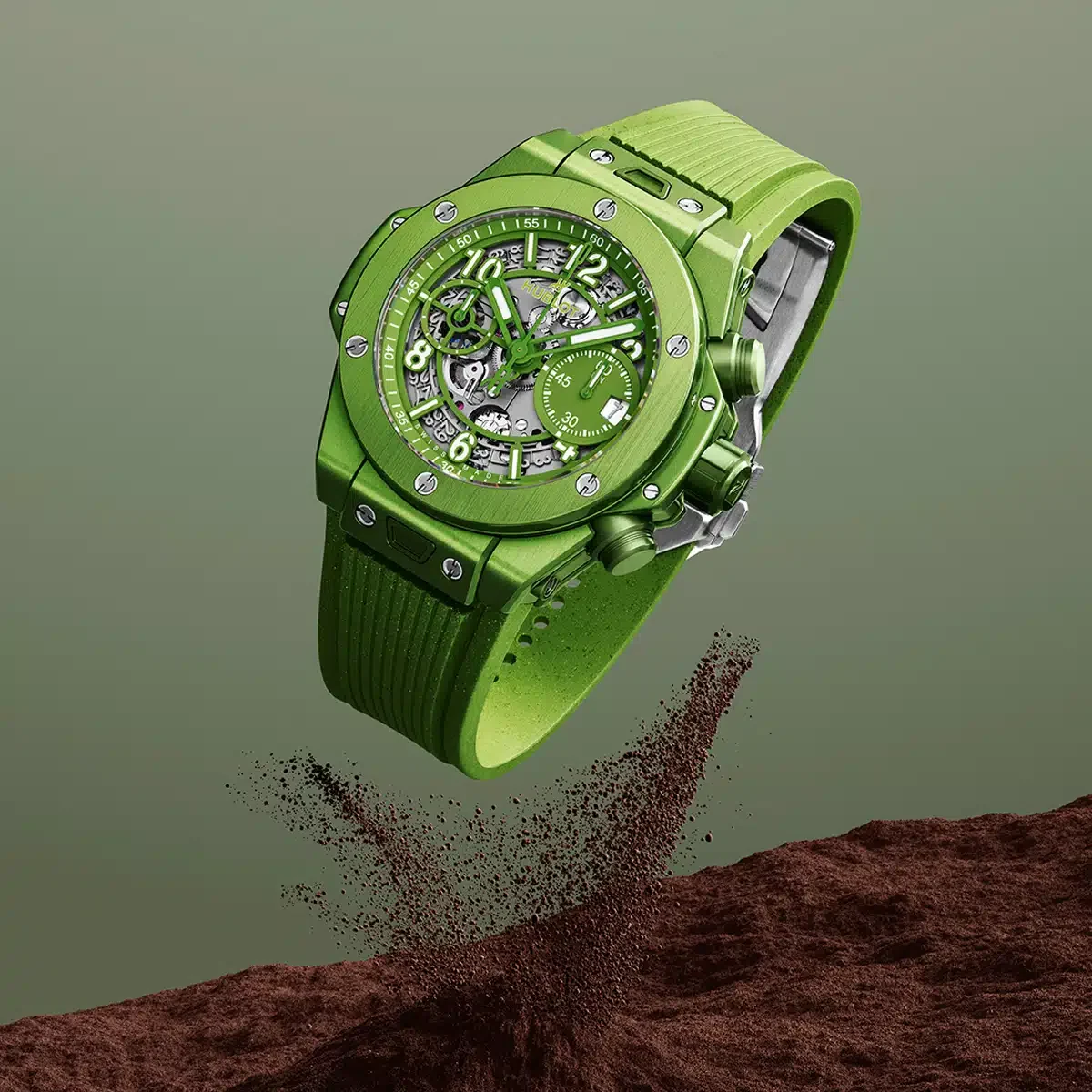 A green Hublot Big Bang Unico Nespresso watch floating above recycled coffee grounds.