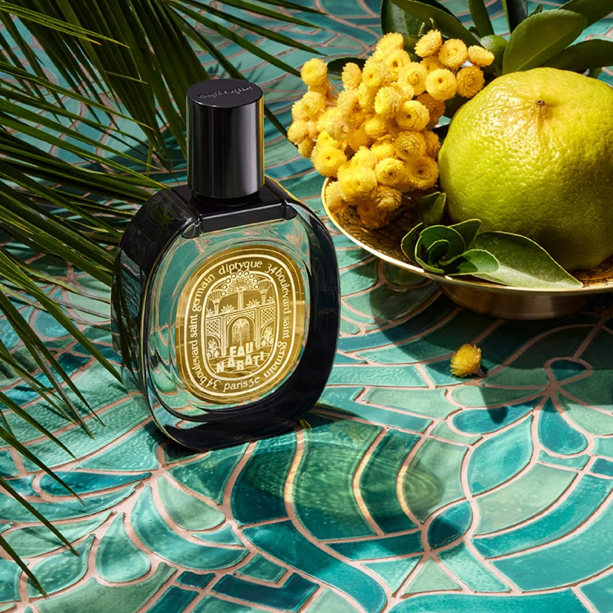 Diptyque Eau Nabati bottle arranged with yellow flowers and citrus.