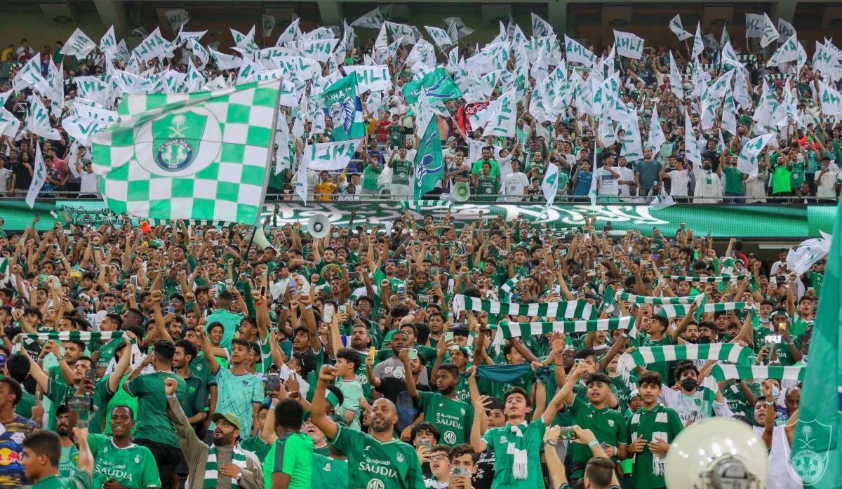 Al-Ahli supporters wave green and white flags inside a packed stadium.