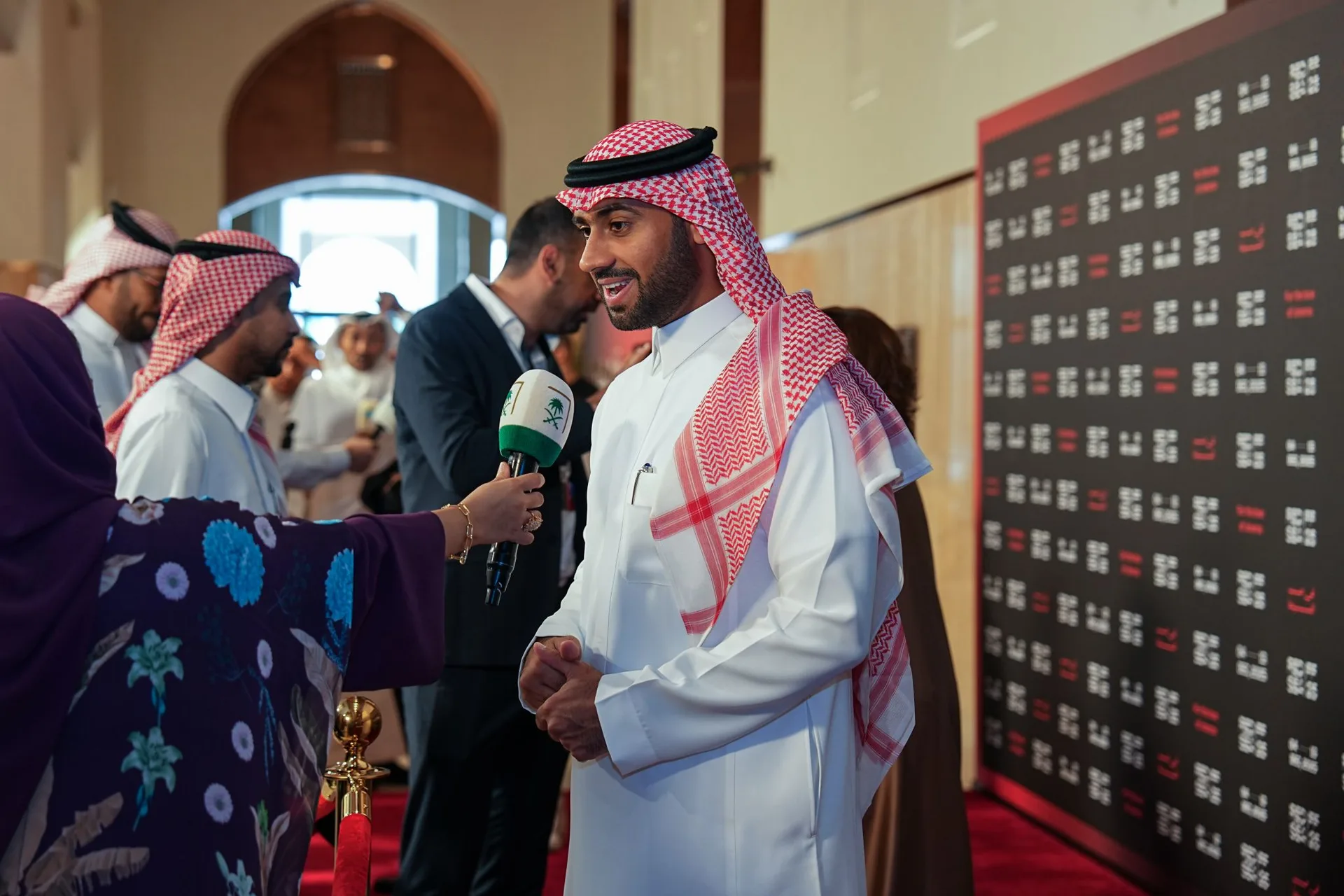 A Red Sea Film Festival spokesperson is interviewed beside the festival media wall.