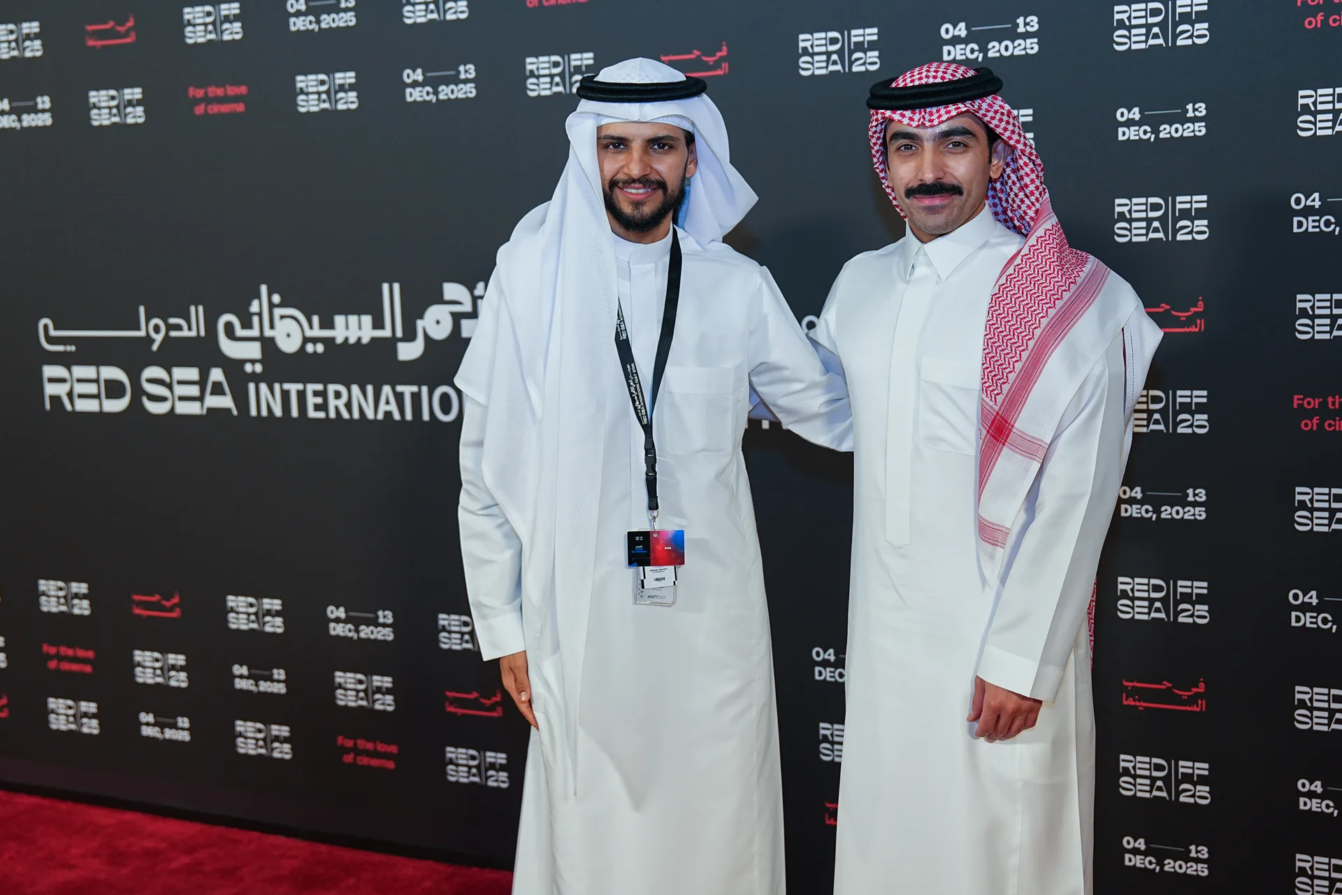 Two men in traditional Saudi dress standing before the Red Sea International Film Festival 2025 media wall.