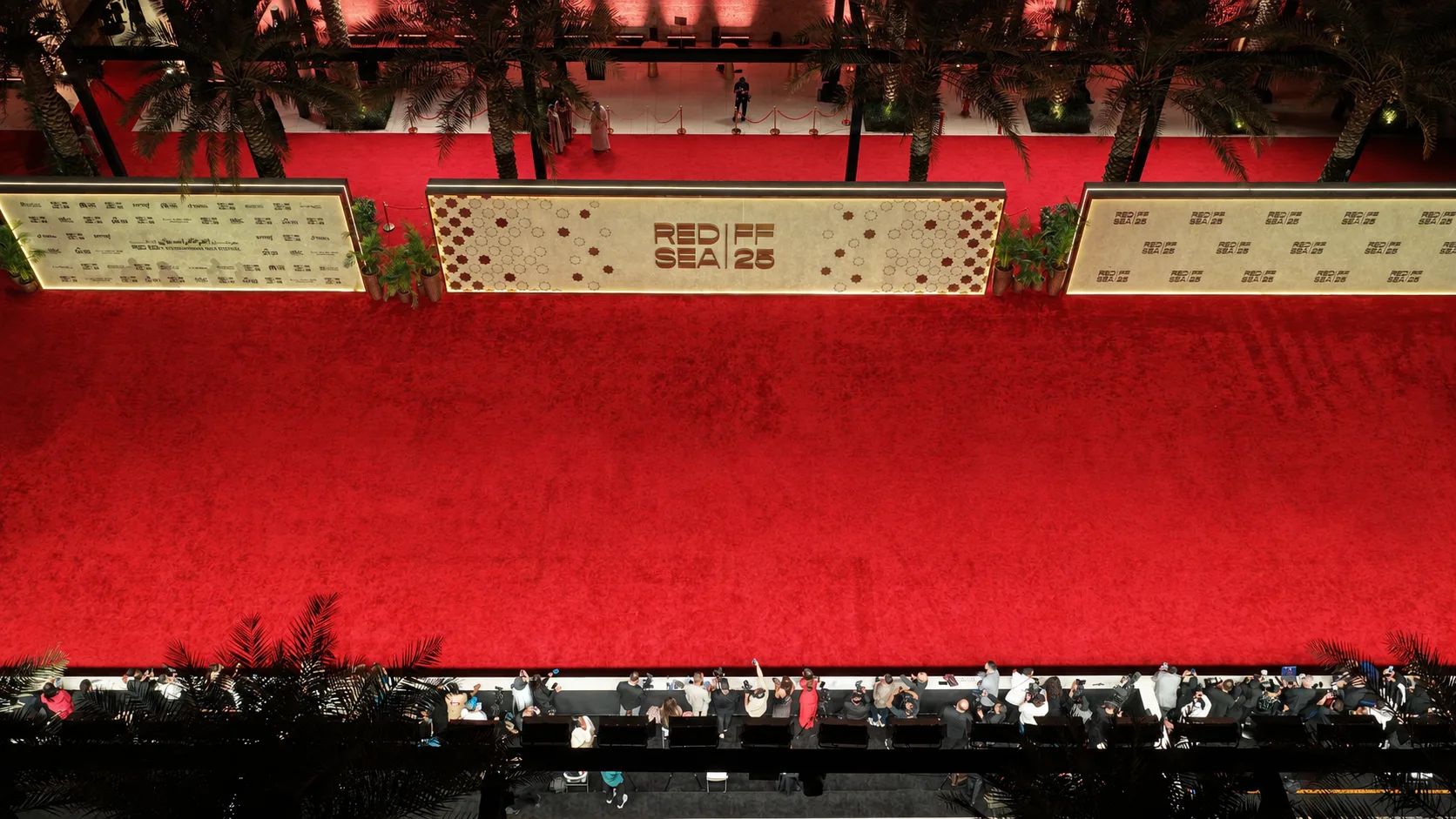 Overhead night view of the Red Sea International Film Festival 2025 venue, with an open red-carpet field between the branded wall and media line.